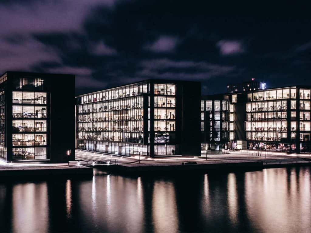 Three large commercial real estate buildings across a river a night